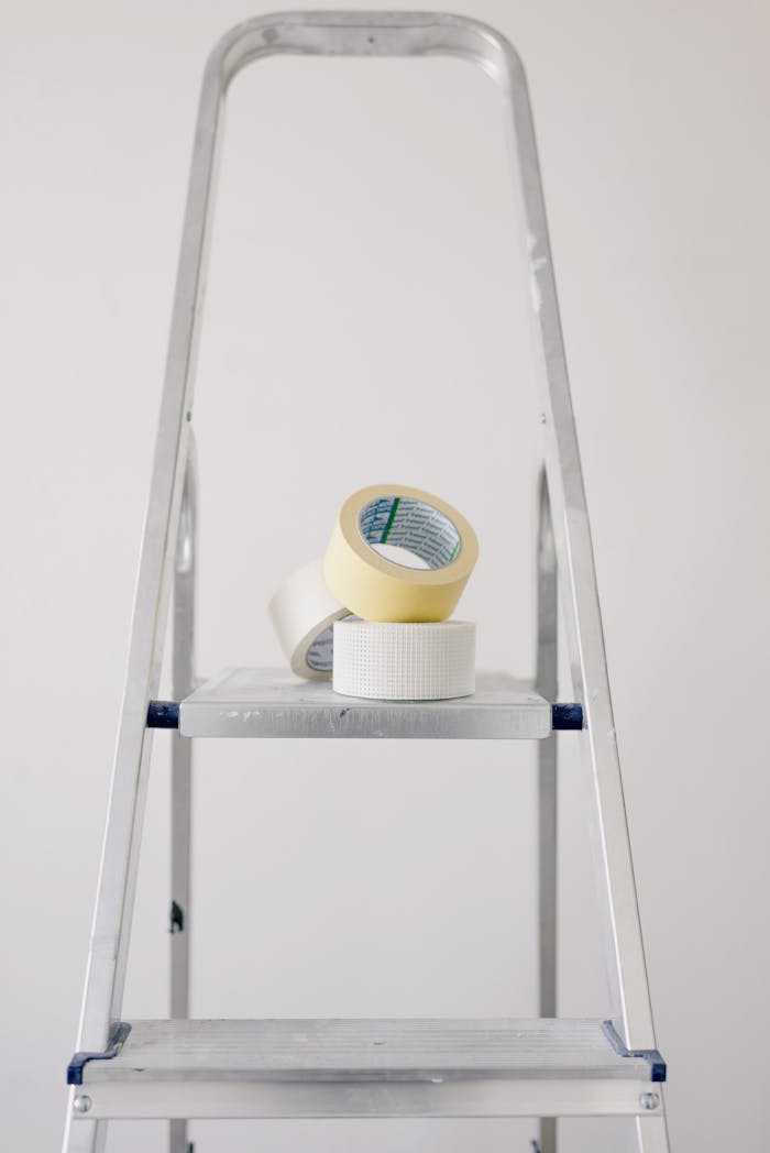 Metal stepladder with rolls of tape for home renovation projects.